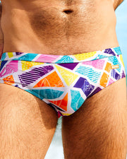  Close-up of a male model wearing MOSAIC Swim Briefs by BANG! Clothing, featuring a vibrant multicolored geometric print. These stylish men's swim briefs are designed for summer beachwear and poolside fashion.