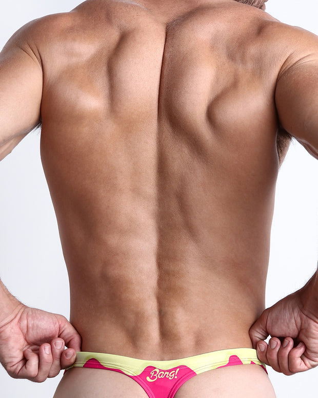 Back view of a Male model wearing beach swim bikini Swimsuit for men in a magenta pink and a pale yellow melting ice cream print by the Bang! Clothes brand of men&