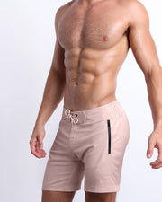 Side view of a male model wearing the men’s NAKED PINK Flex Boardshorts, in a light pink color for men. These premium quality swimwear bottoms are by BANG! Clothes, a men’s beachwear brand from Miami.