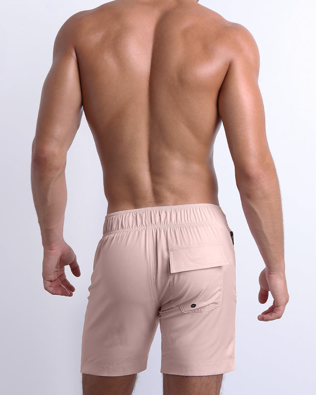 Male model wearing men’s NAKED PINK Flex Boardshorts swimsuit in a light rose quartz pink color, complete with a back pocket, designed by BANG! Clothes in Miami.