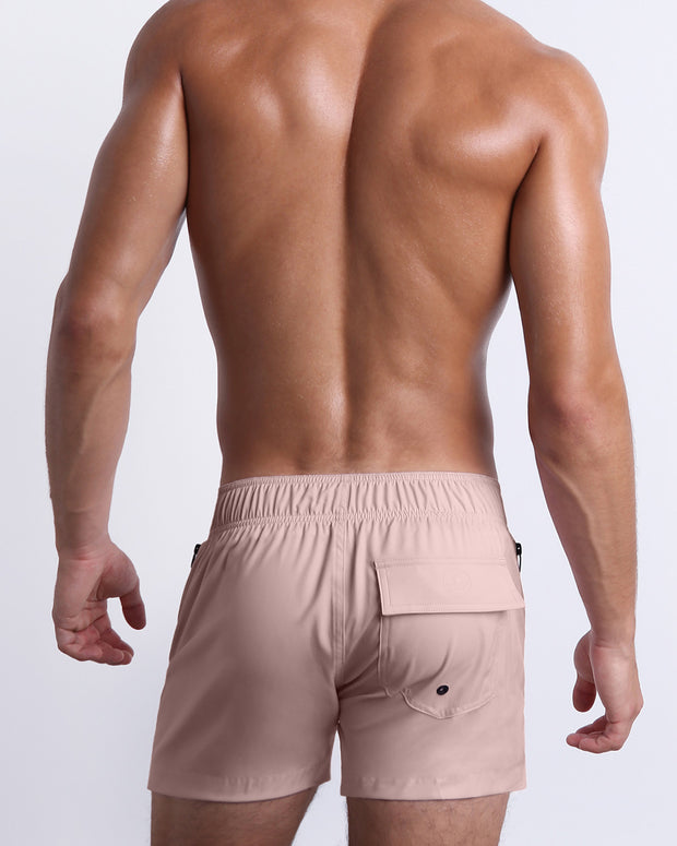 Male model wearing men’s NAKED PINK Summer Flex Shorts swimsuit in a light pink color, complete with a back pocket, designed by BANG! Clothes in Miami.