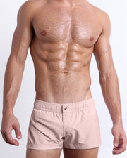 Male model wearing NAKED PINK swimming Mini Shorts, in a light rose quartz pink color for men. These premium quality swimwear bottoms are by BANG! Clothes, a men’s beachwear brand from Miami.