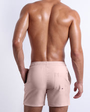 Male model wearing men’s NAKED PINK beach Resort Shorts swimsuit in a light pink color, complete with a back pocket, designed by BANG! Clothes in Miami.