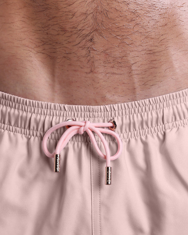 Close-up view of inseam and details of NAKED PINK swimsuit for men, with a light baby pink color cord and custom branded golden cord-ends, and matching custom eyelet trims in gold.