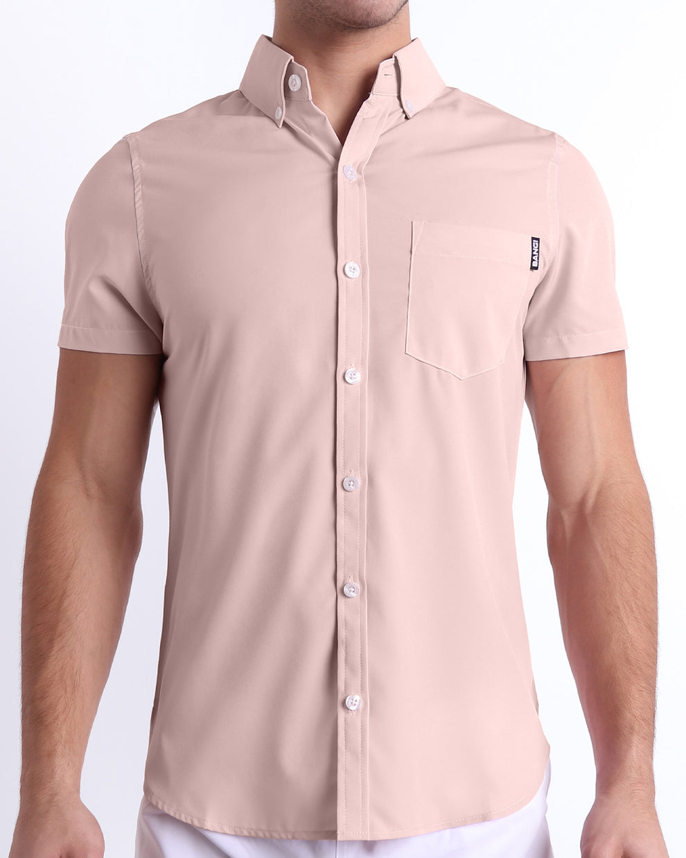 Front view of a sexy male model wearing NAKED PINK men’s short-sleeve stretch shirt, in a light rose quartz pink color for men. This premium quality button-up shirt is by BANG! Clothes, a men’s beachwear brand from Miami.