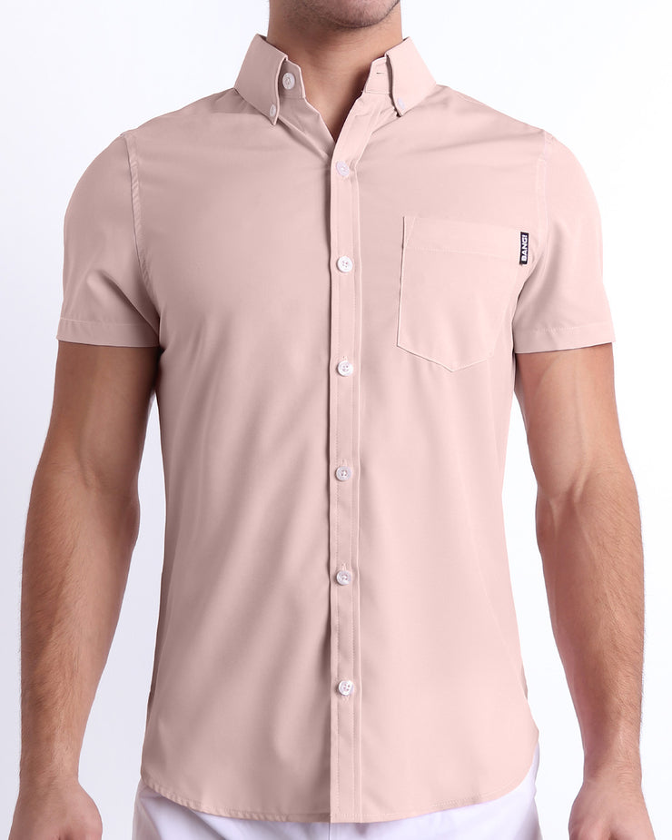 Front view of a sexy male model wearing NAKED PINK men’s short-sleeve stretch shirt, in a light rose quartz pink color for men. This premium quality button-up shirt is by BANG! Clothes, a men’s beachwear brand from Miami.