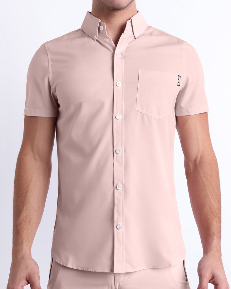 Front view of a sexy male model wearing NAKED PINK men’s short-sleeve stretch shirt and matching shorts for a complete look, in a light rose quartz pink color for men. This premium quality button-up shirt is by BANG! Clothes, a men’s beachwear brand from Miami.