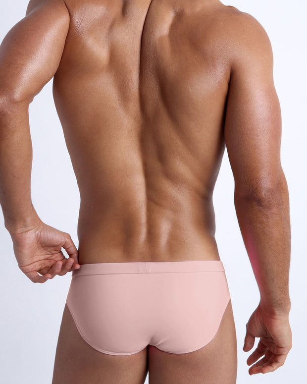 Back view of a male model wearing men’s swim briefs in NAKED PINK a light rose gold color by the Bang! Clothes brand of men&
