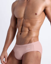 Side view of a masculine model wearing men’s swim European bikini in a light pink color with official logo of BANG! Brand in white.