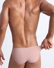 Back view of male model wearing the NAKED PINK beach mini-briefs for men by BANG! Miami in light rose gold pink color.