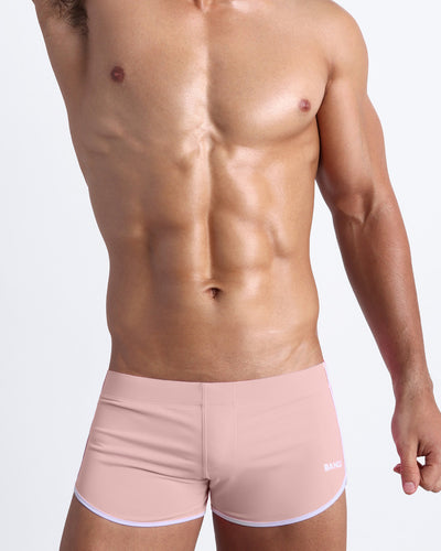 Frontal view of a sexy male model wearing the NAKED PINK men’s swimsuit in a light rose gold pink color by the Bang! Menswear brand from Miami.