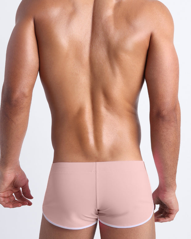 Back view of a male model wearing NAKED PINK men’s swim shorts in a light rose quartz pink color by the Bang! Clothes brand of men&