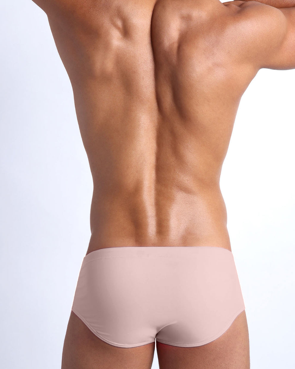Back view of a male model wearing men’s NAKED PINK Brazilian Sunga swimwear in a light rose gold pink color by the Bang! Clothes brand of men's beachwear.