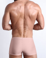 Back view of a male model wearing the NAKED PINK men’s swim trunks in a solid light pink color by the Bang! Clothes brand of men's beachwear from Miami.