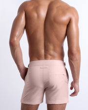 Male model wearing men’s NAKED PINK Summer Tailored Shorts swimsuit in a light pink color, complete with a back pocket, designed by BANG! Clothes in Miami.