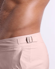 Side view of the NAKED PINK swimsuit Tailored Shorts with dual pockets and adjustable side buckles for men featuring a light rose gold color is designed by BANG! Clothes in Miami.