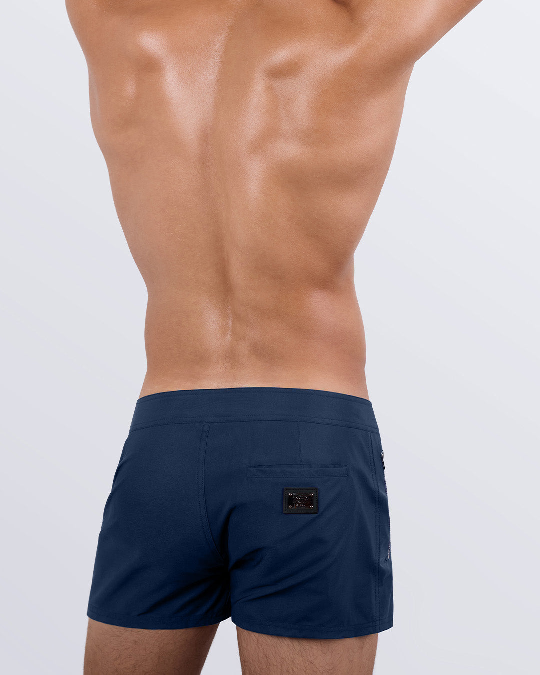 Male model wearing men’s NAVY BOOMER Beach Shorts swimsuit in a dark denim blue color, complete the back zippered pocket, made by DC2 a capsule brand by BANG! Clothes in Miami.