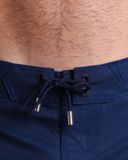 Close-up view of inseam and details of these shorts for men, with navy blue cord and custom branded golden cord-ends, and matching custom eyelet trims in gold.