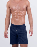 Frontal view of a male model wearing the NAVY BOOMER Flex Boardshorts for men by DC2 Miami. These above-the-knee boardshorts feature a deep navy blue color, a hybrid waistband with a flat front and elasticated back, and an adjustable drawstring for a secure fit. Made from premium, quick-dry fabric, these boardshorts are perfect for beach days, water sports, and tropical vacations.