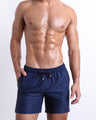 Male model wearing NAVY BOOMER Resort Shorts for men, in a dark navy blue color. These premium quality swimwear bottoms are by BANG! Clothes, a men’s beachwear brand from Miami.