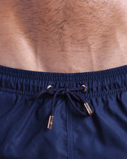 Close-up view of inseam and details of NAVY BOOMER swimsuit for men, with blue cord and custom branded golden cord-ends, and matching custom eyelet trims in gold.