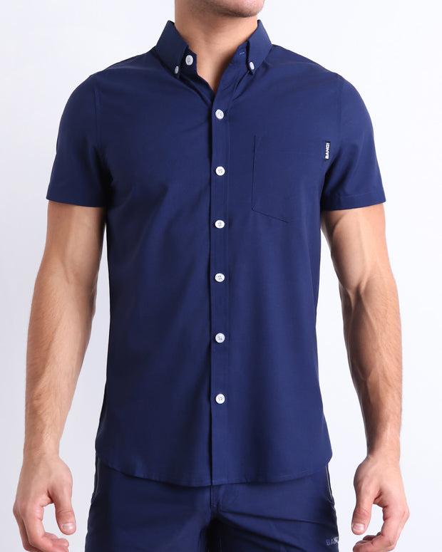 Front view of a sexy male model wearing NAVY BOOMER men’s short-sleeve stretch shirt and matching shorts for a complete look, in a dark denim blue color for men. This premium quality button-up top is by BANG! Clothes, a men’s beachwear brand from Miami.
