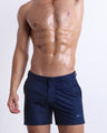 Male model wearing NAVY BOOMER swimming Tailored Shorts, in a dark denim blue color for men. These premium quality swimwear bottoms are by BANG! Clothes, a men’s beachwear brand from Miami.