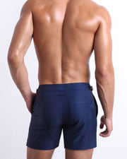 Male model wearing men’s NAVY BOOMER Summer Tailored Shorts swimsuit in a solid dark indigo blue color, complete with a back pocket, designed by BANG! Clothes in Miami.
