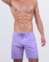 Frontal view of a male model wearing the NEO VIOLET Flex Boardshorts for men by DC2 Miami. These sleek boardshorts feature a modern lavender purple shade, a dual-type "hybrid" waistband with a flat front and an elasticated back, and a functional drawstring for a secure fit. Designed for ultimate flexibility, they are ideal for beach adventures and casual wear.