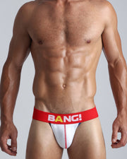 Front view of a sexy male model wearing a BANG! Cotton Jockstrap in OVATION a solid white color with a red waist-band with the BANG! Logo offering a perfect fit.