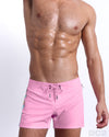 Male model wearing PADAM PINK beach Flex Shorts, premium swimwear in pink with stylish yellow and blue colored stripes for men. These high-quality swimwear bottoms by DC2, a men’s beachwear brand from Miami.