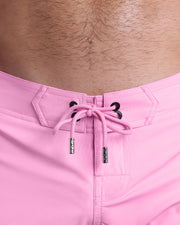 Close-up view of men’s summer Flex shorts by DC2 clothing brand, showing pink color cord with custom-branded golden cord ends, and matching custom eyelet trims in gold.