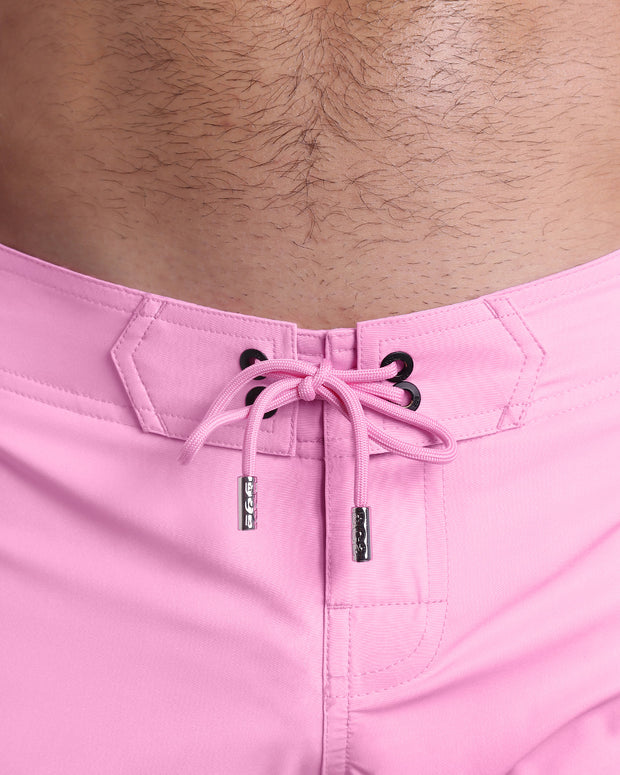 Close-up view of men’s summer Flex shorts by DC2 clothing brand, showing pink color cord with custom-branded golden cord ends, and matching custom eyelet trims in gold.