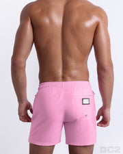 Back view of the PADAM PINK beach Resort Shorts in a solid light pink color with side aqua and pastel yellow stripes for men, complete with a back pocket, designed by DC2.