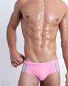Front view of model wearing the PADAM PINK men’s bikini-style Swim Brief, premium swimwear in a solid light pink color with aqua and pastel yellow stripes on the sides for men. These high-quality swimwear are by DC2, a men’s beachwear brand from Miami.
