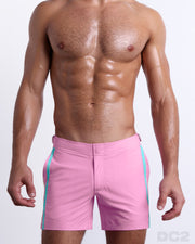 Male model wearing PADAM PINK Tailored Shorts, a solid light pink color with side aqua and pastel yellow stripes for men. These premium quality swimwear bottoms are DC2 by BANG! Clothes, a men’s beachwear brand from Miami.
