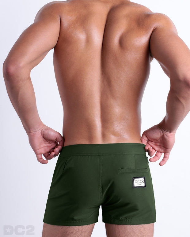 Male model wearing men’s PALM GREEN Beach Shorts swimsuit in a dark pine green color, complete the back zippered pocket, made by DC2 a capsule brand by BANG! Clothes in Miami.