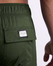 Close-up view of the PALM GREEN men’s Flex Boardshorts back pocket, showing custom branded silver metal logo.