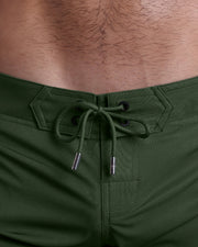 Close-up view of men’s summer Flex shorts by DC2 clothing brand, showing green color cord with custom-branded golden cord ends, and matching custom eyelet trims in gold.