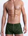 Model wearing the Alpha Green Mini Shorts with a rich olive green finish, elastic waistband with snap-button closure, and a fitted shorter-length silhouette.