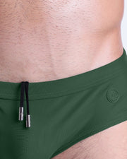 Close-up view of the PALM GREEN men’s drawstring briefs showing black cord with custom branded metallic silver cord ends, and matching custom eyelet trims in silver.