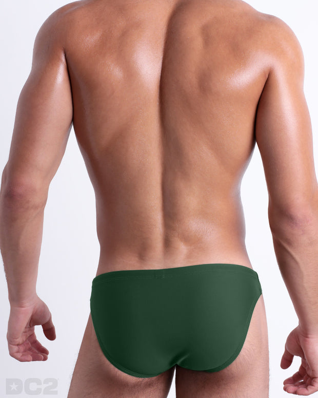 Back view of male model wearing the PALM GREEN beach mini-briefs for men by BANG! Miami in a solid pine green color.