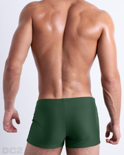 Back view of a male model wearing the PALM GREEN men’s swim trunks by BANG! Miami in a solid pine green color.