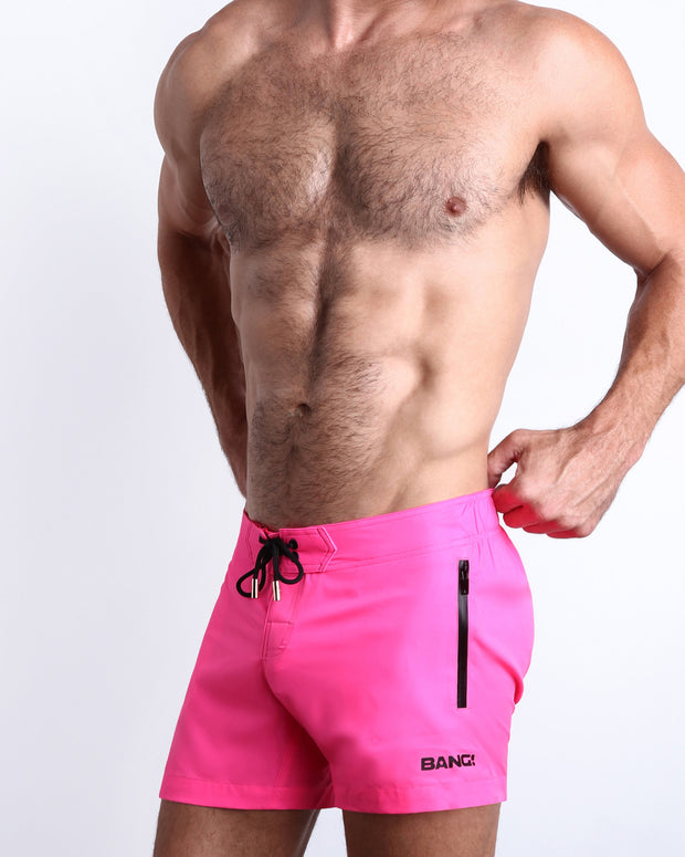 Side view of men’s shorter length swimming shorts in neon pink color with side zipper pockets made by BANG!