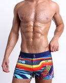 Male model wearing POOL POSITION Beach Shorts, featuring dynamic colors, including shades of blue, red, yellow, and orange. These premium quality swimwear bottoms are by BANG! Clothes, a men’s beachwear brand from Miami.