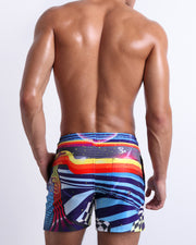 Male model wearing men’s POOL POSITION beach Resort Shorts swimsuit, a racing-inspired design with a burst of colors including blue, red, yellow, and orange is designed by BANG! Clothes in Miami.