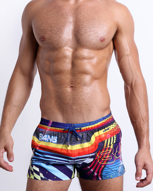 Male model wearing POOL POSITION Show Shorts, featuring dynamic colors, including shades of blue, red, yellow, and orange. These premium quality swimwear bottoms are by BANG! Clothes, a men’s beachwear brand from Miami.