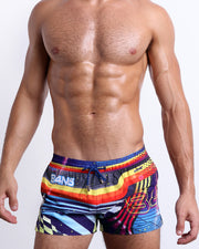 Male model wearing POOL POSITION Show Shorts, featuring dynamic colors, including shades of blue, red, yellow, and orange. These premium quality swimwear bottoms are by BANG! Clothes, a men’s beachwear brand from Miami.