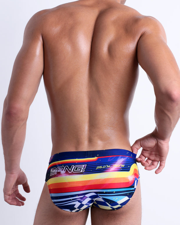 Back view of a model wearing POOL POSITION men’s beach brief featuring a colorful design that pays homage to motorsports and Grand Prix racing, designed by BANG! Clothes in Miami.