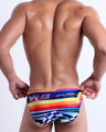 Back view of a model wearing POOL POSITION men’s beach mini-briefs featuring a colorful design that pays homage to motorsports and Grand Prix racing, designed by BANG! Clothes in Miami.